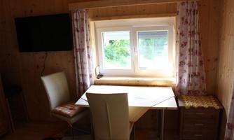 A bright workspace with a table, a chair, and a window. The walls are made of wood, and the room is cozily furnished.