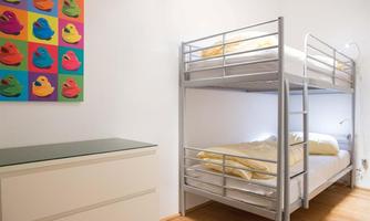 A simple bedroom with a bunk bed and a modern nightstand. On the wall hangs a colorful picture of ducks.