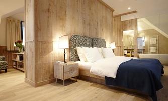 A modern bedroom with wooden paneling and a comfortable bed. The atmosphere is bright and inviting, with soft lighting and elegant decor.