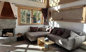 A cozy living area with a large gray sofa and a fireplace. Large windows provide plenty of natural light and create an inviting atmosphere.