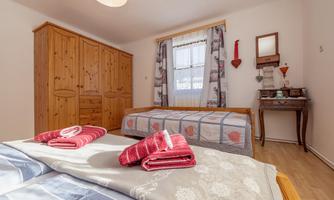 A cozy bedroom with two beds and warm wooden cabinets. There are decorative towels and plenty of daylight coming through the window.