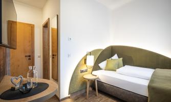 A modern room with a cozy bed and soft colors. The furnishings include a small table and a television.