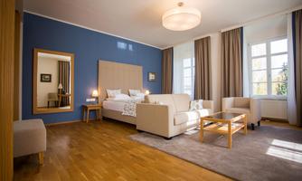 A modern room with a comfortable sofa and two armchairs. The room has large windows, light wooden parquet flooring, and a relaxing atmosphere.