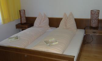 A cozy bedroom with two single beds and decorative pillows. The walls are light, and there are two nightstands with table lamps.