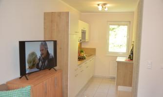 A bright and modern kitchen with an adjoining living room. A TV and a large table are also visible.