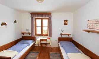 A simple room with two single beds and a small table. The window lets in a lot of light and creates a cozy atmosphere.
