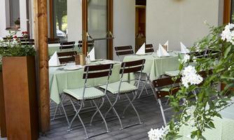 An inviting restaurant with tables in soft green tones and modern chairs. The entrance doors are open and the plants add a fresh touch.