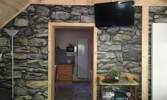 A cozy room with a stone wall and a television. The kitchen is visible in the background.