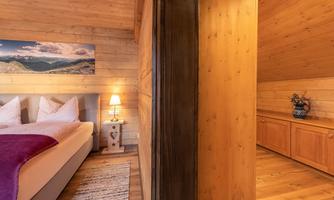 A cozy bedroom with wooden paneling and a comfortable bed.  
In the background, there is a touch of nature, complemented by warm light and wooden details.