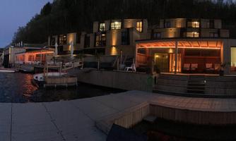 A modern building by the water at dusk. The surroundings are calm and inviting with boats in the harbor.