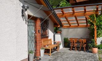 A small house with an inviting terrace. On the terrace, there is a table and chairs, surrounded by plants.