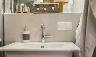 A modern sink in a bathroom with elegant details. On the shelf are care products and a decorative box.