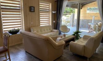 A cozy living room with light wood decor and modern furniture. Large windows provide a beautiful view of the outside area.