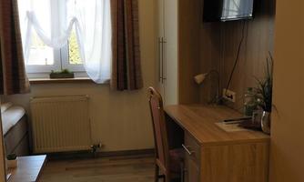 An elegant room with a desk, a chair, and a TV mounted on the wall. Bright curtains let in daylight and create a cozy atmosphere.