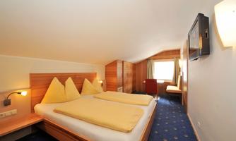A cozy bedroom with two beds and yellow bedcovers. The room is furnished in a modern style and features a television as well as a window with a view outside.