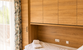 A quiet bedroom with wooden accents and a large window. The bed is unmade with fresh towels on the mattress.