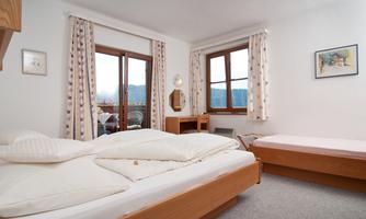A cozy room with a double bed and a single bed. Large windows offer a view of the nature outside.