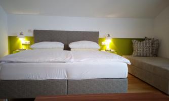 A bright bedroom with a large double bed and a comfortable seating area. The walls are in soft colors, and there are cozy lamps on the nightstands.