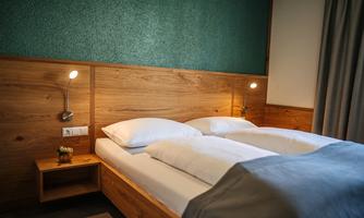 A modern bedroom with two beds and wood-paneled walls. The lighting is soft and the room feels cozy and inviting.