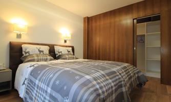 A cozy bedroom with a large bed and stylish pillows. The warm wooden tones and gentle lighting create a relaxing atmosphere.