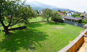A green meadow with some trees and a view of the surrounding hills. In the background, some houses can be seen.