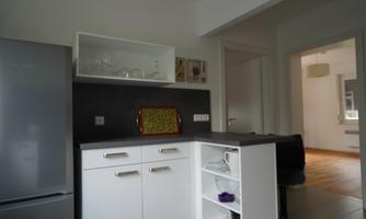A modern kitchen with white furniture and gray countertops. In the background, an open living concept is visible.