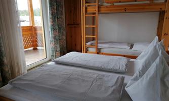 A simple room with a double bed and a bunk bed. Large windows let in plenty of light and display a balcony.