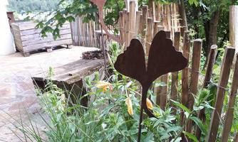 Iron metal figures in the shape of leaves and a fish stand in the garden. They are surrounded by plants and a wooden fence.