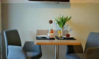 A small dining area with two gray chairs and a wooden table. On the table are a bouquet of flowers, drinks, and fruit.