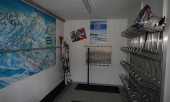 A room with snow sports equipment and a large ski map poster on the wall. On the side, there are ski racks and various ski gear.