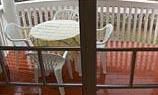 A balcony with a round table and white chairs. The floor is made of wood and it looks like it's raining.