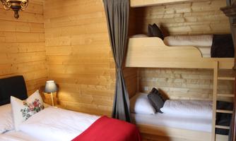 A cozy wooden room with a double bed and a bunk bed. The room has warm tones and a pleasant atmosphere.