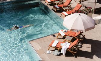 A pool with the clearest water and loungers in a sunny outdoor area. A person is swimming relaxed in the water.