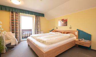 A cozy bedroom with a large double bed and bright walls. The room features a balcony and a pleasant decor.