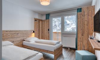 A cozy room with two wooden single beds. Large windows offer a view of the snowy landscape outside.