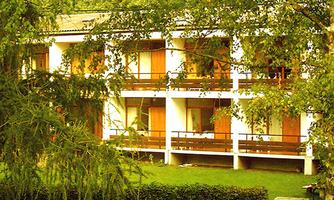 A building with several floors and balconies, surrounded by trees. The garden is well-maintained and provides a peaceful atmosphere.