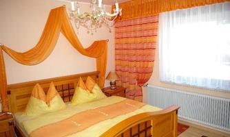 A cozy bedroom with a wooden bed and yellow-orange bedding. The walls are adorned with orange curtains and decorative elements.