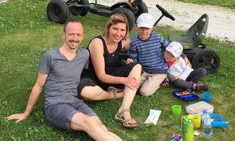 A family sits on the grass and enjoys a relaxing day outdoors. In the background, there are go-karts.