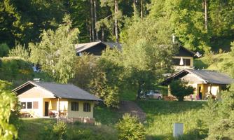 A peaceful landscape with several small holiday homes, surrounded by trees and green areas. The houses are arranged on a gentle slope.