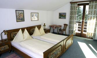 A cozy bedroom with two single beds and decorative headboards. Large windows provide plenty of daylight and access to a balcony.
