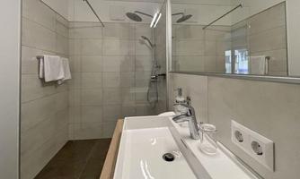 A modern bathroom with an open shower and a sink. The walls are brightly tiled and the design is simple and elegant.