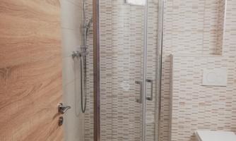 A modern bathroom with a shower and a toilet. The walls are clad with a light tile pattern.