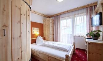 A cozy bedroom with wooden furniture and a red carpet. Large windows let in plenty of light.
