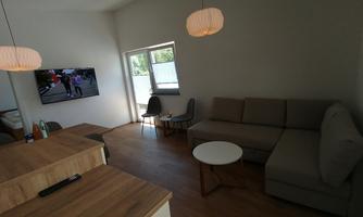 A modern living room with a large window and a television. A comfortable sofa and a table complement the space.