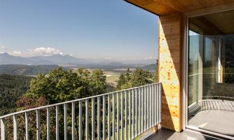 A modern terrace overlooking a picturesque landscape and mountains in the background. The sky is clear and sunny, perfect for relaxing outdoors.