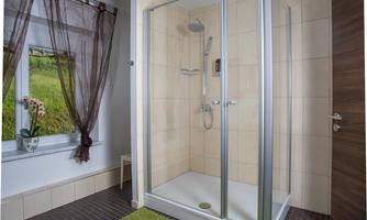 A modern bathroom with a glass shower. The floor is covered with a green carpet and there is a window overlooking nature.