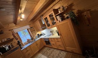 A cozy wooden kitchen with modern appliances. There is a large windowsill and a beautiful carpet on the floor.
