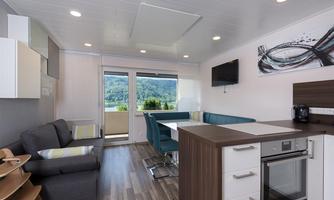A modern and bright kitchen and living unit with a view of nature. There is a comfortable sofa, a dining table, and a fully equipped kitchenette.