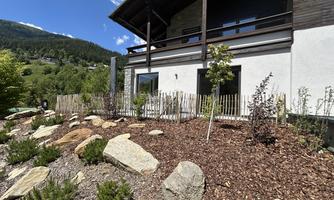 A modern house with a balcony and a beautiful view of the mountains. The garden is beautifully landscaped with stones and plants.