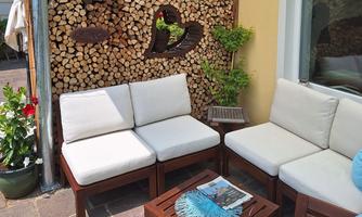 A cozy seating area with white furniture and a small wooden table. In the background, there is a decorative wall made of wooden logs.
